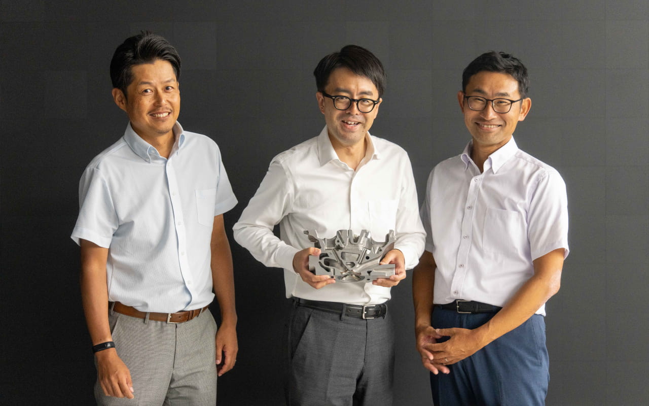 Members of the team hold a cross-section of the cylinder head from the ZR15DDTe engine